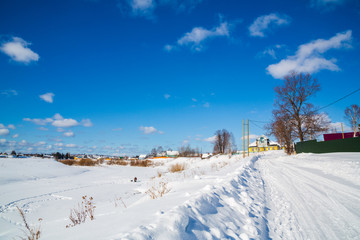 Winter landscape. Countryside. Snowy road. Sunny day. Blue sky. White clouds.