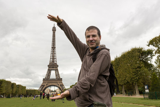 Tourist plays with Eiffel tower in the city of Paris on cloudy day.