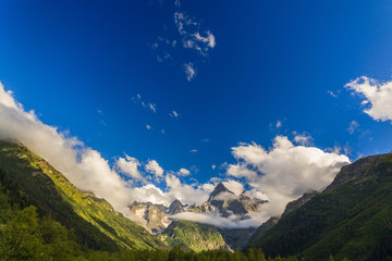 Naklejka premium Clouds over the tops of the rocky mountains overgrown with trees. Photographed in the Caucasus, Russia.