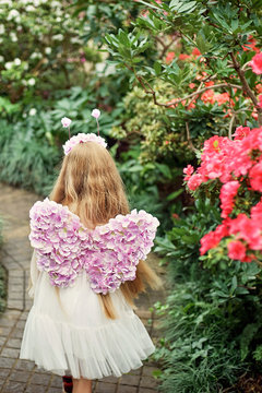 girl sniffing flowers of azaleas. flowering azaleas in the park. Girl with violet butterfly wings. Fantastic photo shoot. magic fairy costume and flower crown. The concept of childhood and holiday.