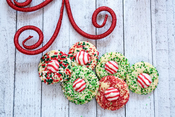 Homemade peppermint kisses Christmas cookies with colorful sprinkles (jimmies) over a wood background with decorative festive holiday elements