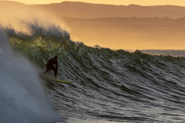 Silhouette of a surfer riding a wave at sunrise at Jeffreys Bay, South Africa