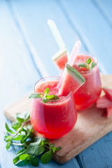 Tasty cold watermelon smoothie drink with mint in glasses, summer refreshing cocktail on wooden background