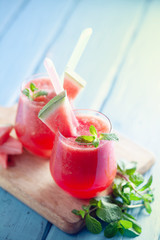 Tasty cold watermelon smoothie drink with mint in glasses, summer refreshing cocktail on wooden background