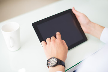 Close-up of businessman changing online data on tablet. Unrecognizable employee sitting at table with mug and using portable computer. Technology concept