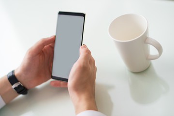 Close-up of businessman holding gadget with blank screen. Man sitting at table and using mobile app on smartphone. Message concept