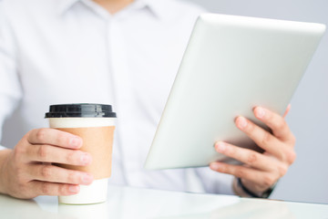 Close-up of businessman using table and drinking coffee from disposable cup. Unrecognizable manager analyzing online report in office. Lifestyle concept