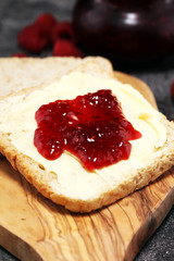 Toast bread with homemade raspberry jam or marmalade on rustic table served with butter for breakfast or brunch
