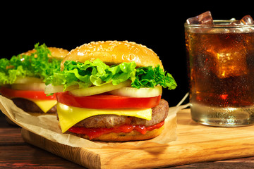 Sandwich with cutlet, cheese, tomatoes, onion, salad, ketchup and a glass of Coca Cola on a wooden...