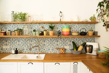 Fototapeta na wymiar Stylish open space kitchen with accessories, plants and plates. Design interior of cozy kitchen. Mosaic backgrounds wall. 