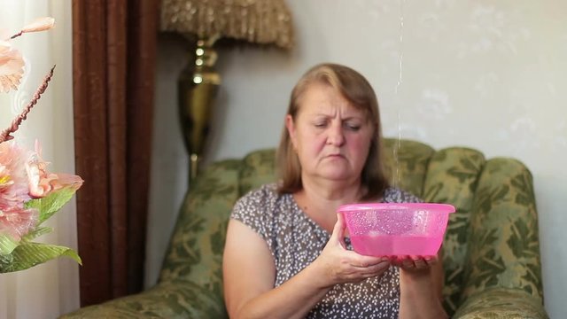 Agitated woman holding the dishes while water drops dripping from the ceiling