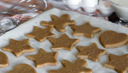 Dough for cookies in the form of stars and hearts on parchment baking paper.