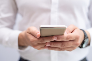 Close-up of young businessman networking on mobile phone. Caucasian man reading message or browsing on smartphone. Mobile communication concept