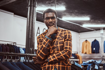 Fototapeta na wymiar Elegantly dressed African man posing with hand on chin while standing in a classic menswear store.
