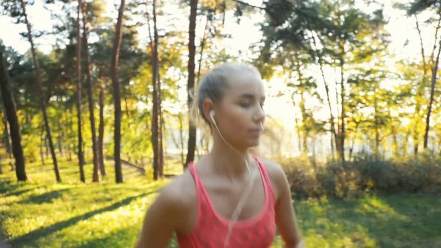 Slim fair-haired woman going for a morning run, wearing cute salmon top and listening to music as exercising, outdoor shot on great fall day