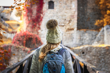 Fototapeta na wymiar Hiking woman is going to castle ruins over wooden bridge. Tourist in autumn season. 