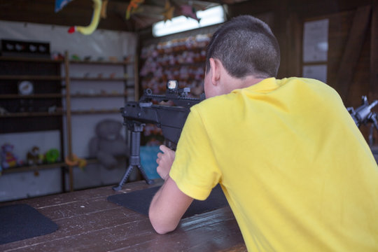 Caucasian teenage boy aiming with black pneumatic rifle in a shooting galery, rear view