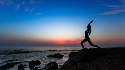 Silhouette of young woman doing exercises on the Sea during amazing sunset.