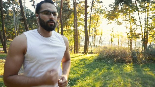 Intelligent black-haired man going jogging in beautiful green park, outdoor shot on sunny fall day in the sunset
