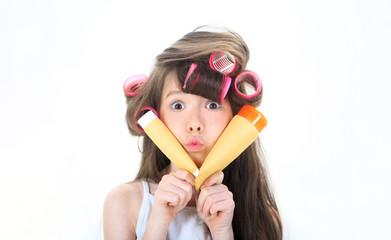 Kid fashion, cosmetics. Cute teen putting cream on her face. Little girl is holding a tube for the cream. Skincare, cosmetics, facial treatment. Little girl in hair curlers. Teen in hair curlers.