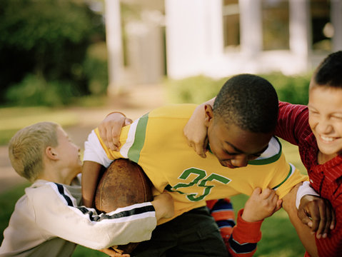 Three Boys Playing A Friendly Game Of Football In The Back Yard.