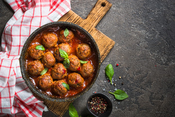 Meatballs in tomato sauce in a frying pan on dark stone table. 