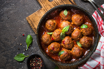 Meatballs in tomato sauce in a frying pan on dark stone table. 