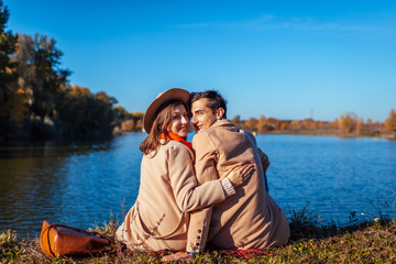 Young couple in love chilling by autumn lake. Happy man and woman enjoying nature and hugging