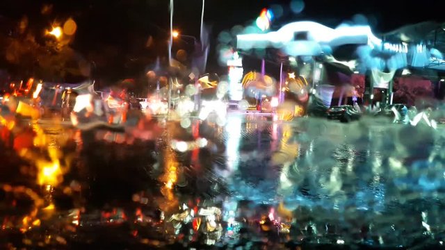 Traffic stands still, on a cold, wet day, shot through a windscreen, focusing on the rain droplets, tailights out of focus
