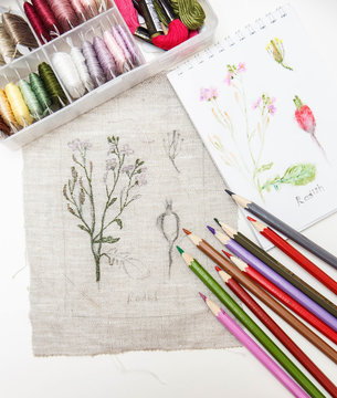 Embroidery in process with sketch, pencils and sewing threads on table