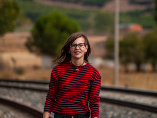 Portrait of a teenage girl with glasses and casual clothes walking on the train tracks
