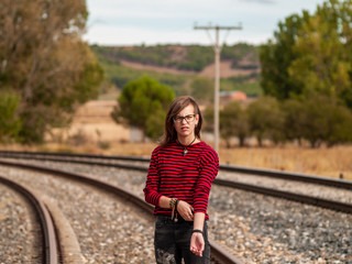 Portrait of a teenage girl with glasses and casual clothes walking on the train tracks