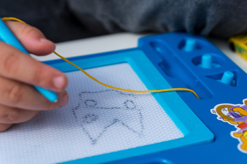 Photo of a kid drawing on a magnetic drawing board. Education process concept. Learning to draw....