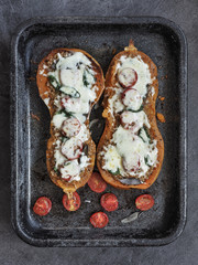 Baked halves of pumpkin stuffed with crushed meat, tomatoes and cheese. Seasonal meal. Overhead shot.