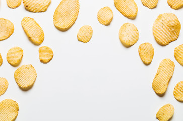Crispy potatoes chips isolated on white background. Food background. Potato chips lying at a distance from each other on a white table with empty center.