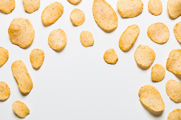 Crispy potatoes chips isolated on white background. Food background. Potato chips lying at a distance from each other on a white table with empty center.