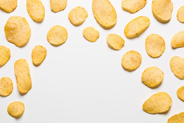 Crispy potatoes chips isolated on white background. Food background. Potato chips lying at a distance from each other on a white table with empty center.
