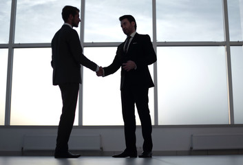 businessmen shake hands, standing near a large office window