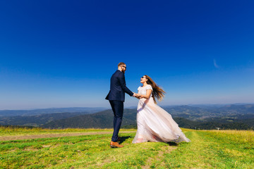 Newlyweds stand opposite one and hold hands and smile through su