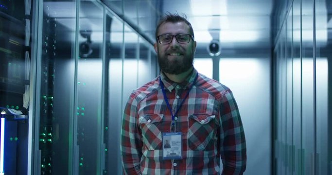 Portrait of adult bearded man glasses standing in corridor of server room in data center smiling at camera