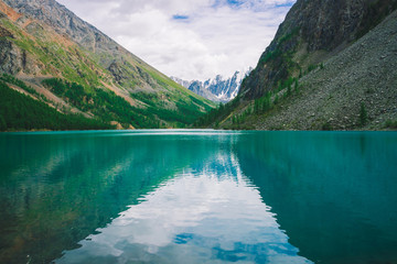 Shine water in mountain lake in highlands. Wonderful giant snowy mountains. Creek flows from glacier. White clear snow on ridge. Amazing atmospheric landscape of majestic nature.