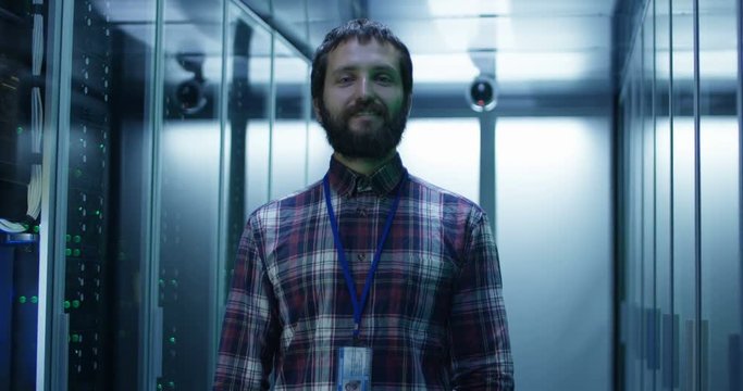 Portrait of adult bearded man standing in corridor of server room in data center smiling at camera