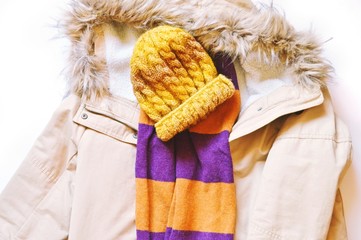 Beige women's winter jacket with a hood, a yellow knitted wool hat and a stylish striped scarf. Flat lay winter season fashion photo