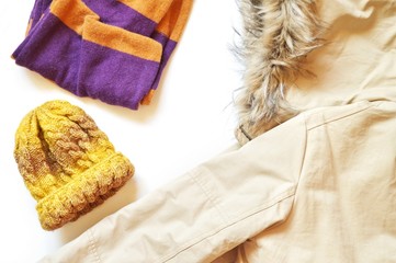Striped scarf, yellow wool hat and beige park jacket with faux fur. Flat lay winter fashion photo