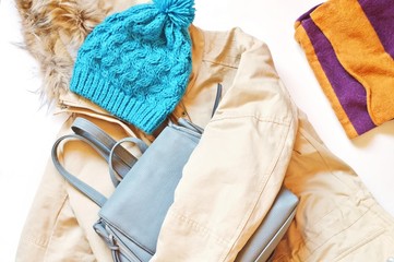 Women's beige winter jacket with faux fur collar, blue knitted hat, striped scarf and backpack. Flat lay fashion outfit