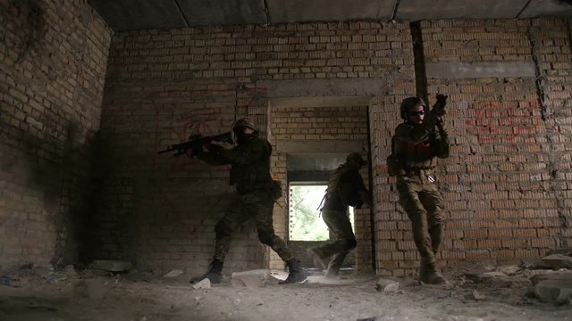Squad of special forces marines with weapons storming building occupied by enemy during anti terrorism operation. Army soldier securing the rear of squad while jumping enemy targets on battlefield.