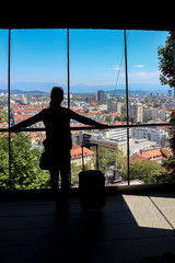 Silhouette of a girl with a suitcase against the background of the city in the window