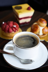 Breakfast time with cup of hot coffee and pieces of cream cake with strawberries and raspberries, sweets dessert breakfast snacks, close-up. Berry cupcakes dessert on wooden table background, top view