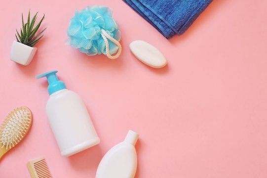 Bath products for body and hair care on a pink background. Organic shampoo, herbal shower gel, natural soap, wooden comb and blue terry towel. Flat lay photo