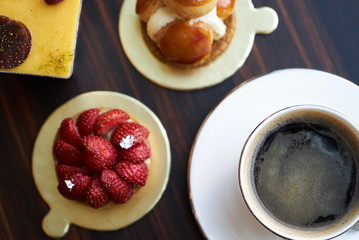 Breakfast time with cup of hot coffee and pieces of cream cake with strawberries and raspberries, sweets dessert breakfast snacks, close-up. Berry cupcakes dessert on wooden table background, top view